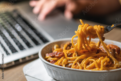 Fényképezés Eating spaghetti while working on laptop at home