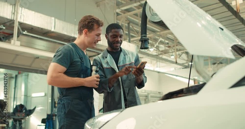 car mechanics standing in front of broken car using mobile phone concept of online mobile repair service booking using application Modern technology Men browsing fix problem at workshop, first helper