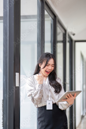 A beautiful and cheerful Asian businesswoman or female boss is showing her clenched fist and looking at her tablet with an excited face, receiving good news and achieving goals Free Download A beautiful and cheerful Asian businesswoman or female boss is showing her clenched fist and looking at her tablet with an excited face, receiving good news and achieving goals - GFXLoad