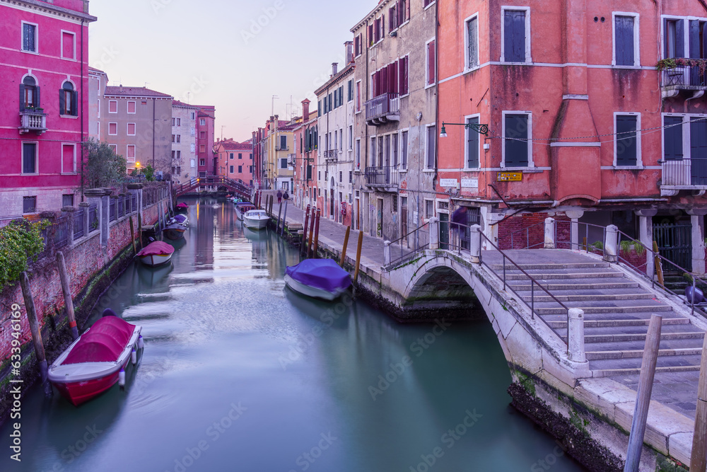 Sunrise of canal, boats, bridge, and street name signs, Venice