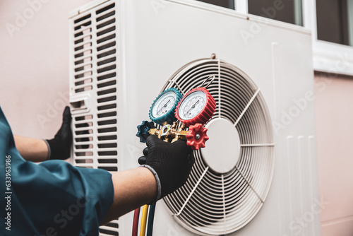 Heat and Air Conditioning, HVAC system service technician using measuring manifold gauge checking refrigerant and filling industrial air conditioner after duct cleaning maintenance outdoor compressor.