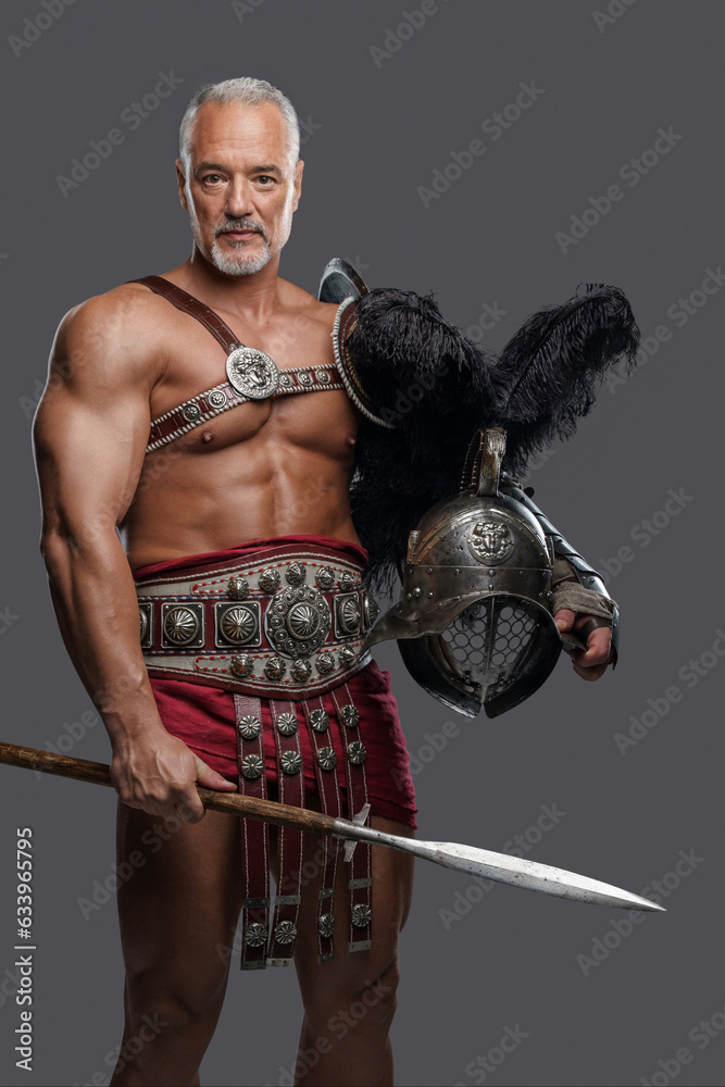Regal and stoic elderly warrior, dressed in historical armor, holds his spear and helmet, standing strong and proud on a plain grey backdrop