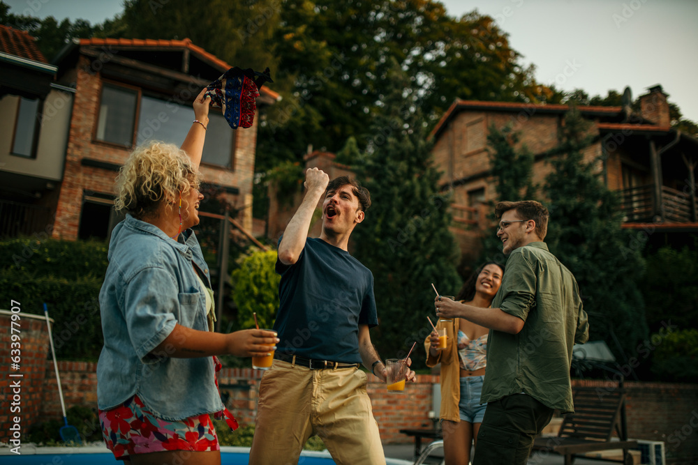 Happy friends dancing and enjoying pool party at poolside.