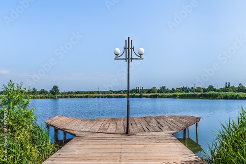 Single street lamp on a wooden pier on the lake in Trostyanets central park, Sumy region, Ukraine. One lantern in the middle of the bridge against the background of the blue water surface of the pond photo