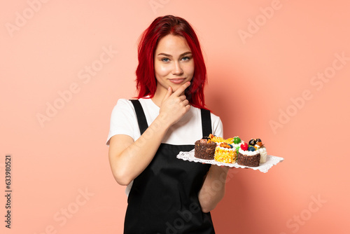 Pastry chef holding a muffins isolated on pink background thinking