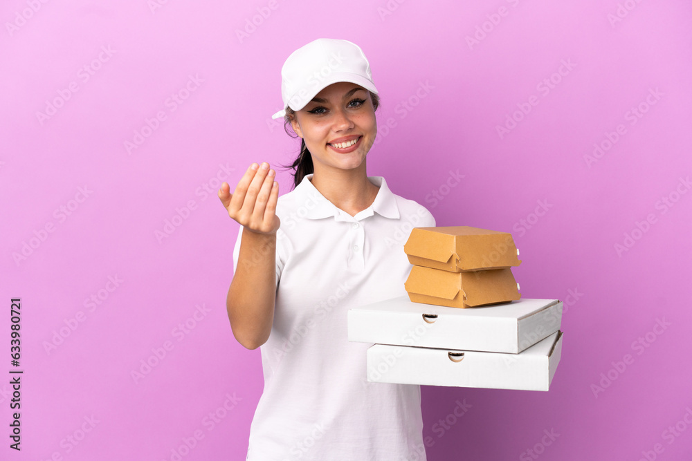 Pizza delivery Russian girl with work uniform picking up pizza boxes and burgers isolated on purple background inviting to come with hand. Happy that you came Pizza delivery Russian girl with work uniform picking up pizza boxes and burgers isolated on purple background inviting to come with hand. Happy that you came