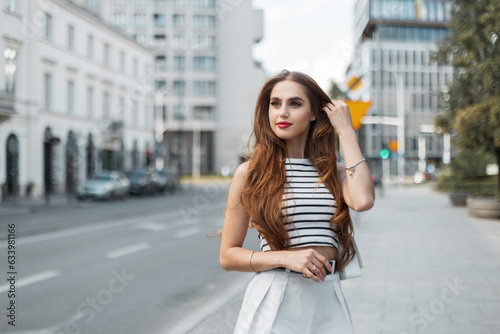 Happy beautiful fashion woman with red lips walking in the city near the road