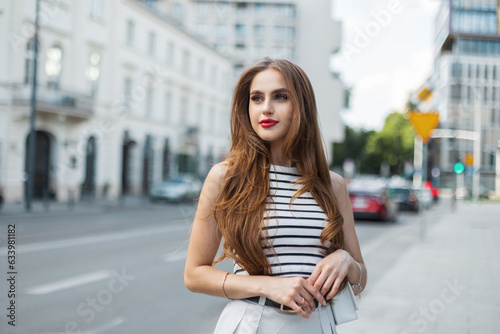 Beautiful young brunette girl model in fashionable summer casual clothes with a handbag walks in the city