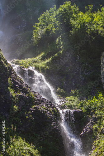 A beautiful waterfall of Polikara flowing down a steep slope on a sunny clear day among green plants in Krasnaya Polyana in Russia and a space for copying