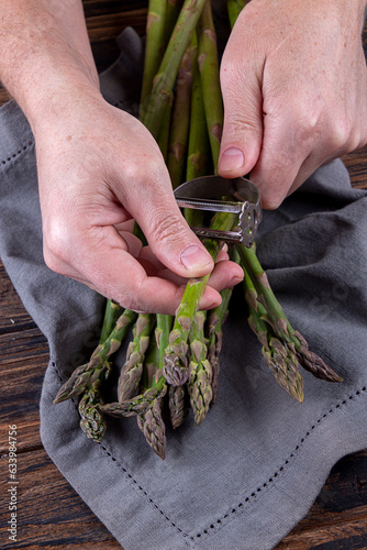 Man peeling green asparagus. Wooden background. Men's hands and organic fresh asparagus