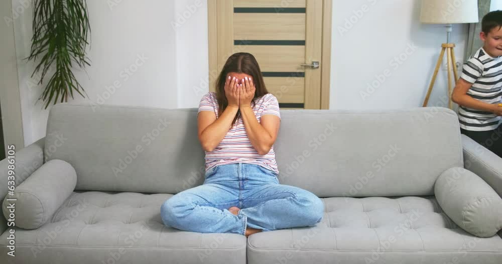 Mother sitting on couch, feeling tired of active children playing running around Mother sitting on couch, feeling tired of active children playing running around