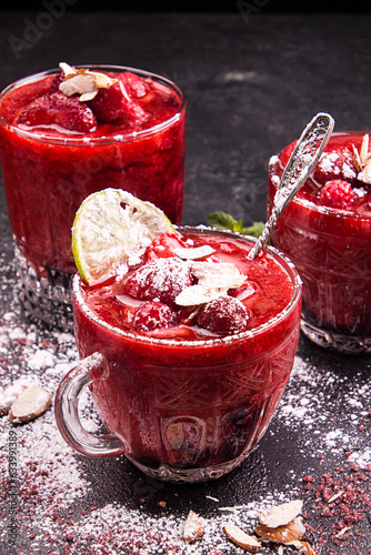 Blended strawberry shake smoothie with whole strawberries, ice and lemon in glasses on black background.