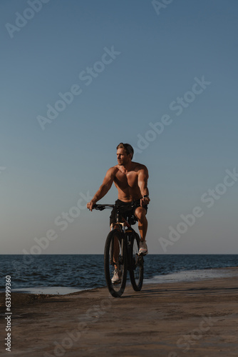 Handsome young shirtless man enjoying summer morning while cycling seaside