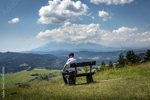 A man sitting on a wooden bench, watching a mountain landscape at Wysoki Wierch, Pieniny Mountains, Poland. 