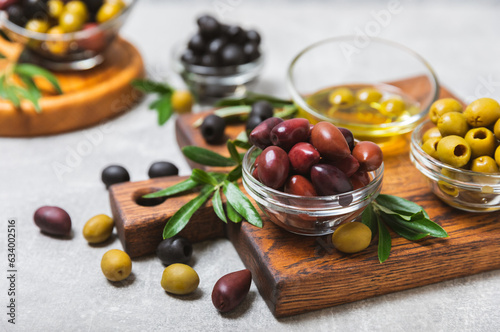 A set of green, red and black olives on a light marble background. Various types of olives in bowls and fresh olive leaves. Vegan. Olive fruits. Place for text. Copy space.