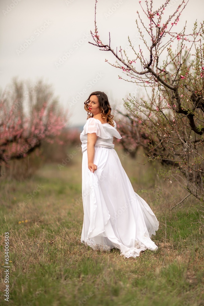 Woman peach blossom. Happy woman in white dress walking in the garden of blossoming peach trees in spring