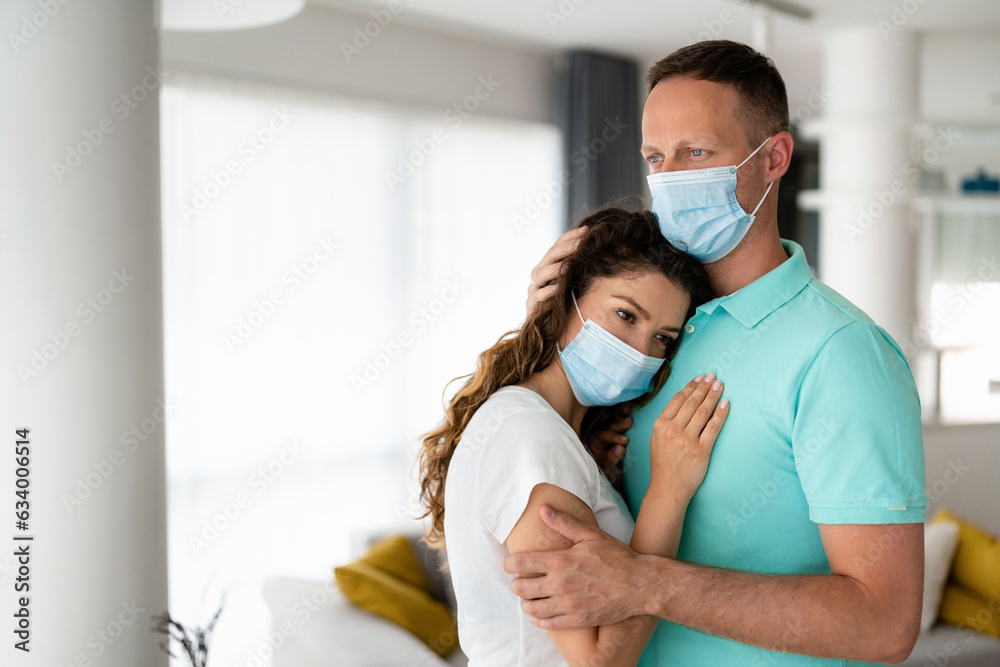 Sad anxious woman leaning against her worried and disturbed husband's chest with masks on. Man embracing his sick woman.