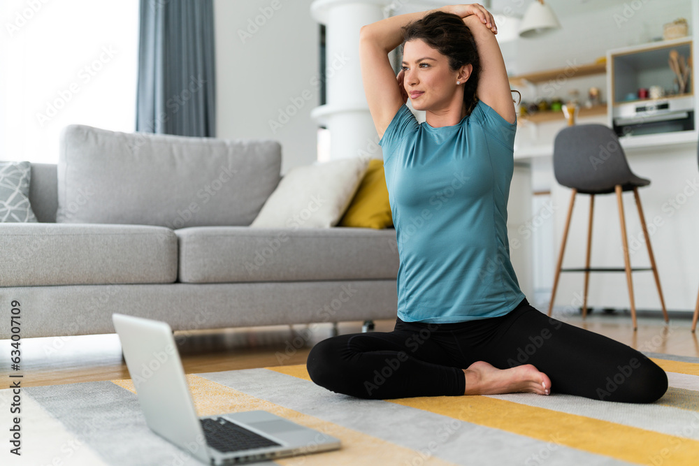 Young athlete woman in sporty clothes training on floor at home and watching videos on laptop. Young athlete woman in sporty clothes training on floor at home and watching videos on laptop.