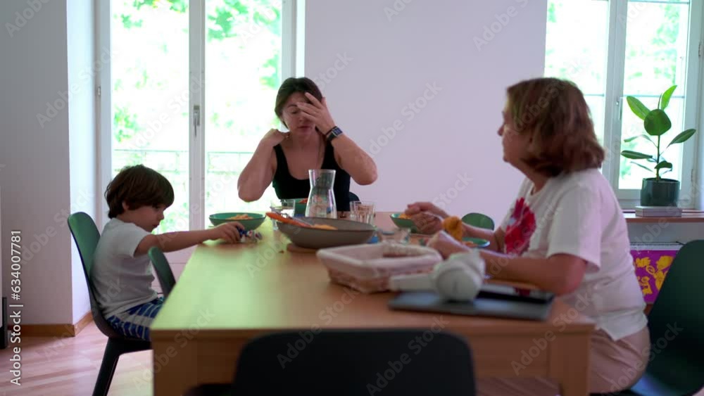 Candid family scene lifestyle at home, casual elderly woman with adult woman and child sitting at lunch table eating meal Candid family scene lifestyle at home, casual elderly woman with adult woman and child sitting at lunch table eating meal