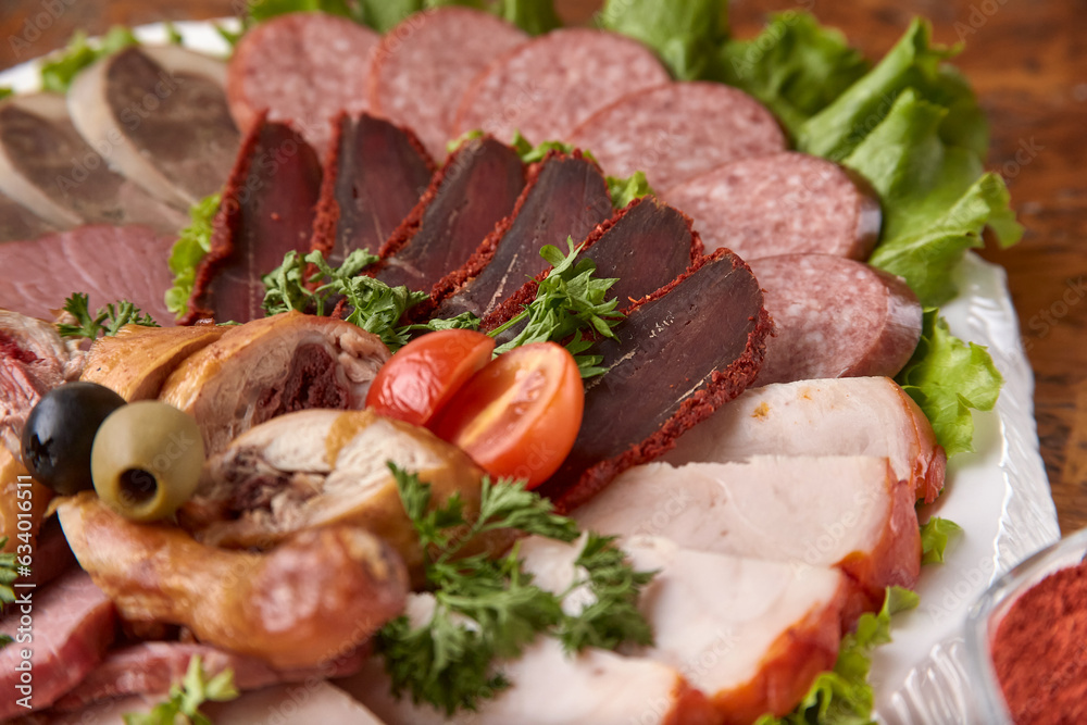 Part of plate with cold cuts with choice - salami, pieces of sliced ham, sausage, chicken, qazi horse meat, tomatoes on salad, close-up, shallow depth of field