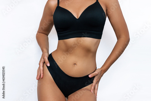 Cropped shot of young slim tanned woman in black underwear demonstrating her hourglass figure with toned abs isolated on white background. Result of fitness, diet, healthy lifestyle. Girl perfect body