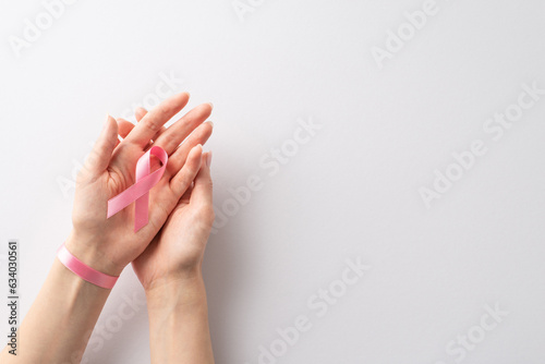 Remembering Breast Cancer Awareness Month. From above, female hands cradling a pastel pink ribbon on a white isolated background. Versatile for promotional content or text messages