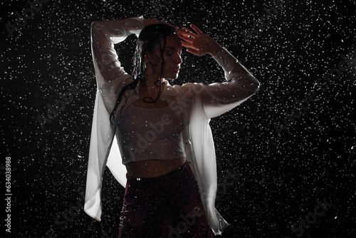 Dancing in the rain. A young woman in wet clothes dancing among water droplets, photo in the aqua studio. beautiful silhouette, model in a white shirt © Ulia Koltyrina