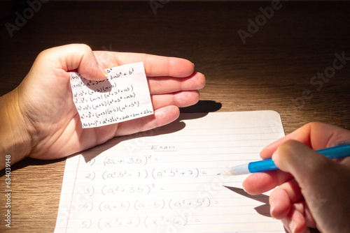 Student using formula math sheet to cheat on test. Hand of university student holding pencil doing math question in examination and cheating with answer piece of paper in hand