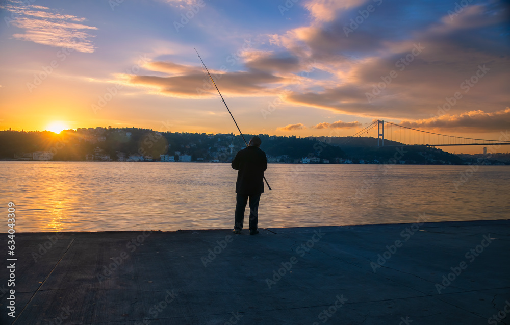 Fisherman with rod fishing on the sea. Fisherman with bridge view and sunset in the background. 