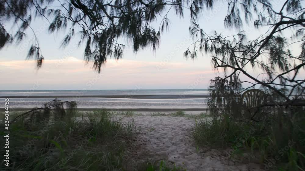 Aerial drone pushing in towards green trees to reveal a serene Australian sandy low tide beach with calm blue ocean, vibrant blue sky and fluffy pink clouds at sunset Aerial drone pushing in towards green trees to reveal a serene Australian sandy low tide beach with calm blue ocean, vibrant blue sky and fluffy pink clouds at sunset
