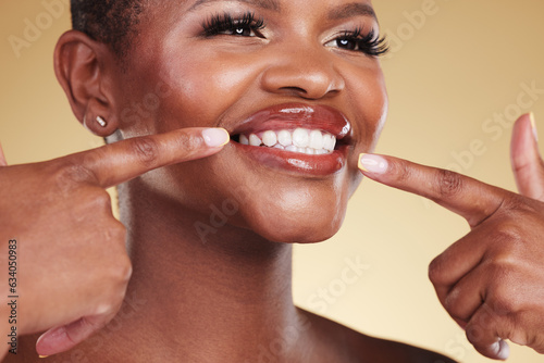 Smile  beauty and a woman pointing at teeth in studio with skin care  glow and makeup. Face of an African model person with dental shine  dermatology and cosmetics announcement on a beige background