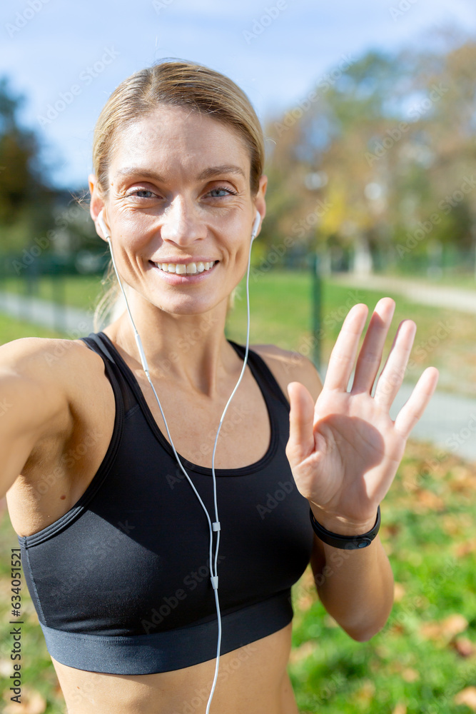Female athlete after jogging in stadium talking with friends and recording online video blog, mature blonde with headphones looking at smartphone camera smiling, video call with headphones Female athlete after jogging in stadium talking with friends and recording online video blog, mature blonde with headphones looking at smartphone camera smiling, video call with headphones
