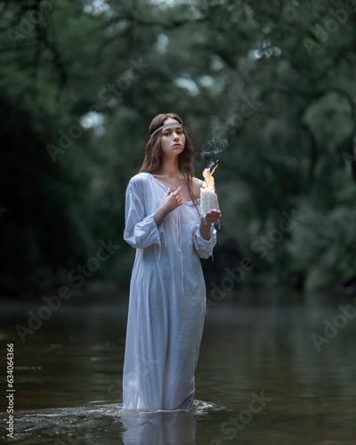 Girl in a Slavic white shirt with burning candles in a forest river photo