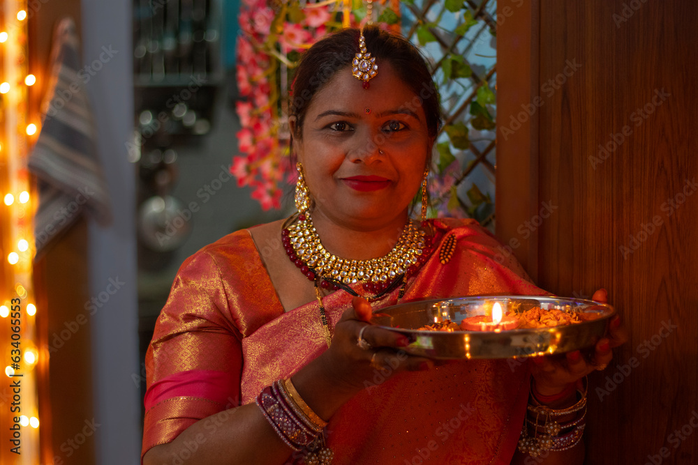 portrait of a happy young woman standing with diyas at home during diwali celebration