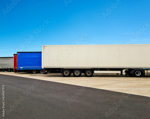 Trucks of international transport stand parallel to each other in a parking lot near the autobahn. Asphalt, bright blue sky. Mock up, copy- space. Minimalism.
