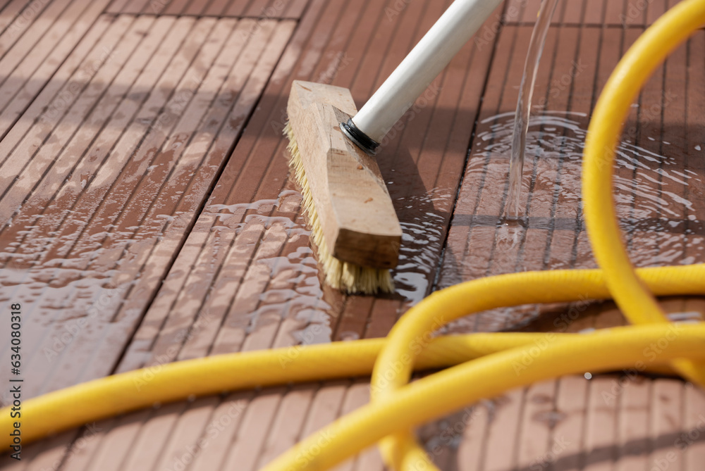 Detail of a scrubbing brush and a water hose during spring cleaning of a wooden terrace floor