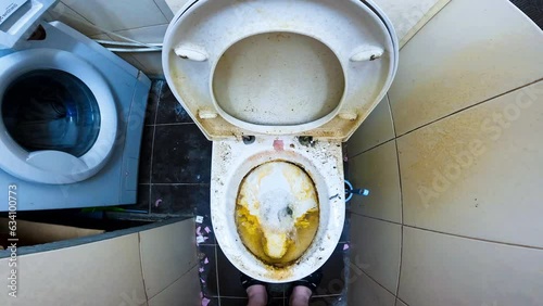 Water is pouring close-up into very dirty toilet bowl with traces of limescale and rust. Lid of a dirty toilet bowl. Dirty tiled bathroom, washing machine, toilet. Dirty tiles on the floor and walls photo