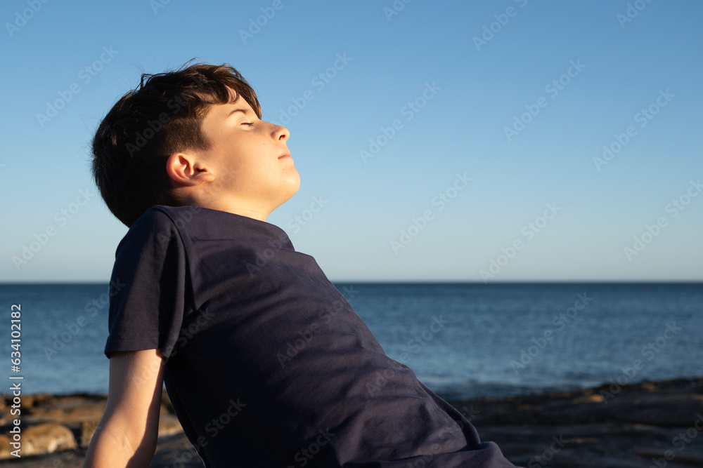 Young kid enjoying good weather on the coast, shore, breathing deep fresh sea air with eyes closed during sunset Young kid enjoying good weather on the coast, shore, breathing deep fresh sea air with eyes closed during sunset