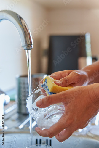 Woman washing glass cup with sponge and detergent in kitchen