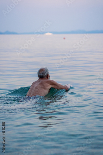 Aged man swims in the Adriatic sea. Gray haired man swimming in tranquise water of sea an sunset time.