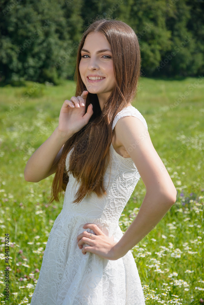 Beautiful young smiling woman in a flowery meadow in a white dress