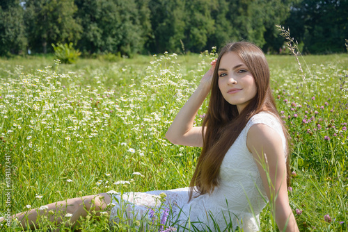 Obraz na płótnie Beautiful young woman sits in a flowery meadow in a white dress w salonie