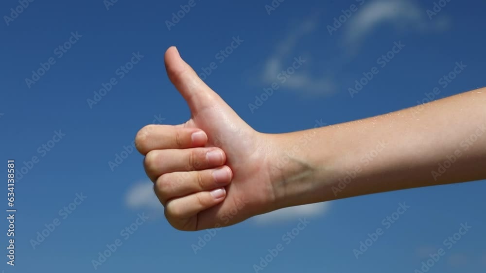 Child shows a thumbs up gesture against the blue sky, a concept on the theme of clear sunny weather Child shows a thumbs up gesture against the blue sky, a concept on the theme of clear sunny weather