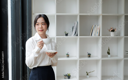 Young beautiful Asian businesswoman having a coffee during a coffee break in her own office room.