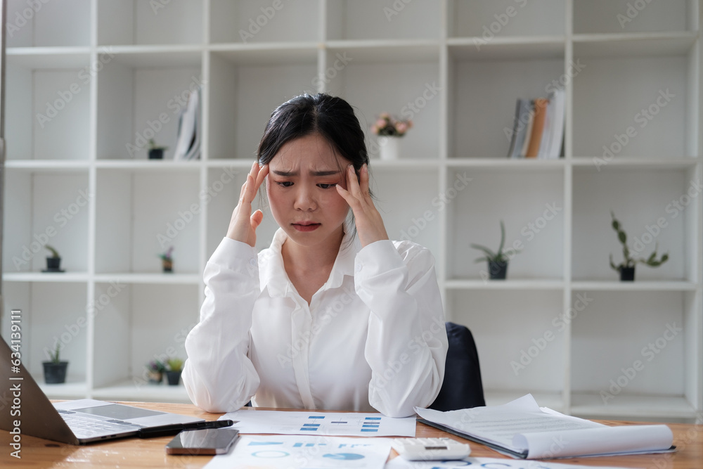 Stressed and exhausted young Asian businesswoman having a headache from the overloading assignment. Stressed and exhausted young Asian businesswoman having a headache from the overloading assignment.