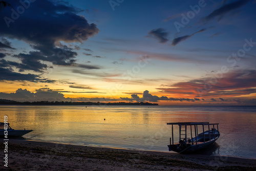 Fototapeta Naklejka Na Ścianę i Meble -  A colorful sunset at Gili Air beach in Indonesia. Calm sea, blue evening sky, red-orange sky and silhouettes of people