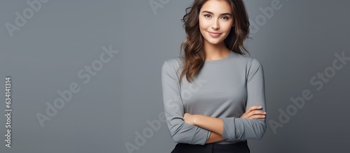Smiling young woman with stylish outfit poses on grey background holding hands in pockets looks at camera copy space