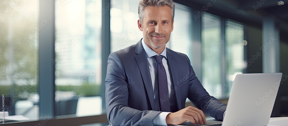 Fototapeta premium Middle aged professional sitting at desk in office working on laptop and taking notes
