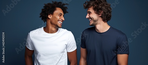 Two young men in their 20s wearing white casual shirts are happily talking together in a studio portrait with a dark blue background photo