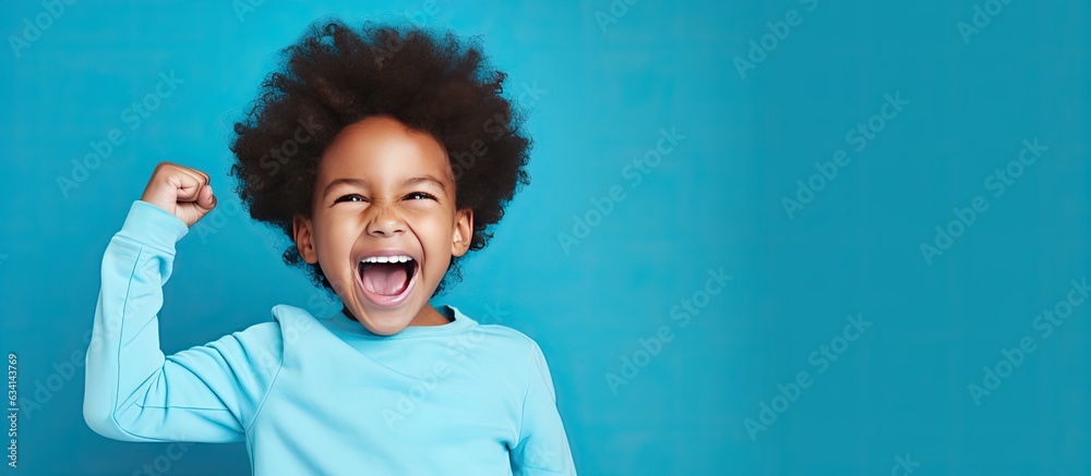 Victorious black boy celebrating with joy standing in blue studio